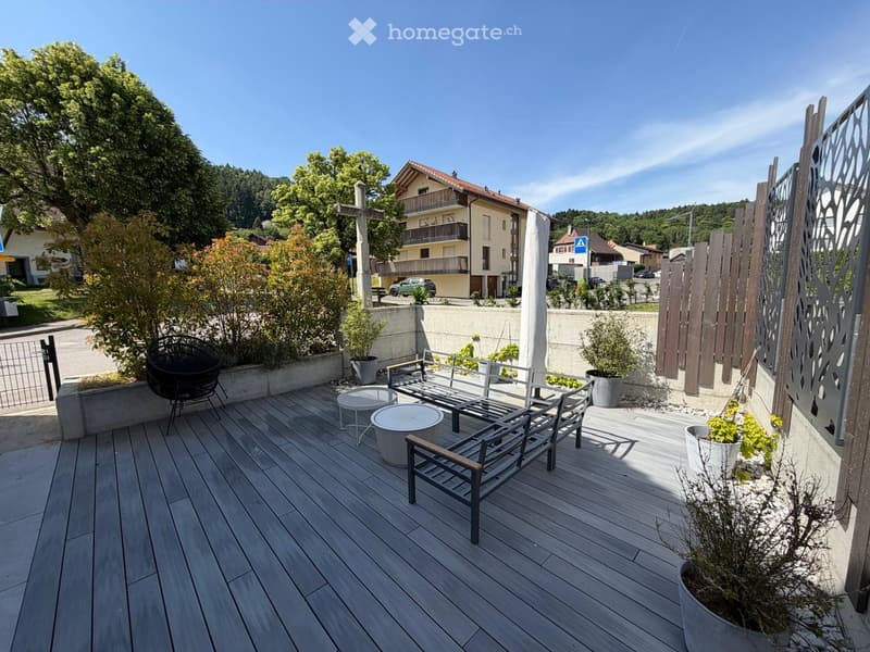 Wooden deck with a bench, chairs, tables, and potted plants, overlooking a residential area with houses and trees.