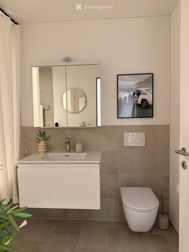 Modern bathroom with a white sink, mirror cabinet, toilet, and a framed picture on the wall. The space features beige tiles and a sleek design.