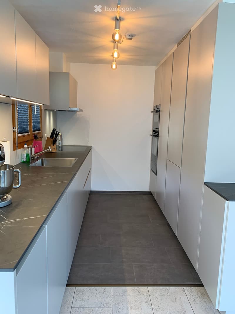 Modern kitchen with white cabinets, dark countertops, stainless steel appliances, and a built-in oven. Features a sink, mixer, and knife block on the counter.
