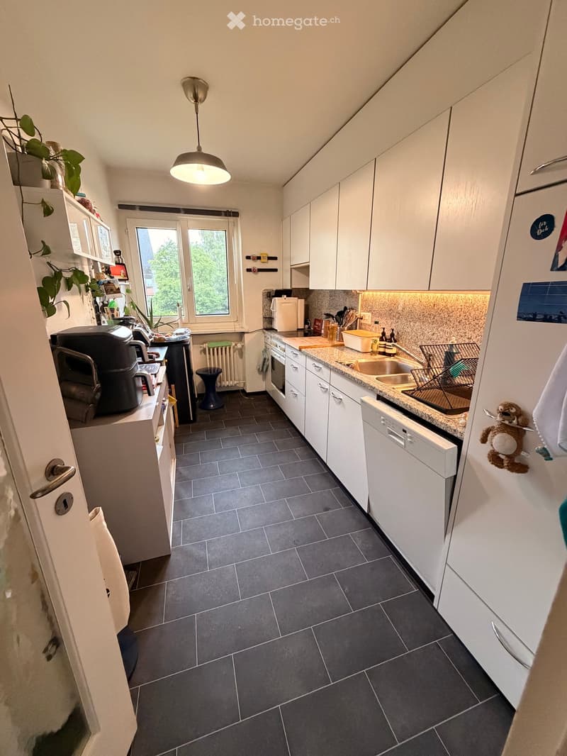 Modern kitchen with white cabinets, dark tiled floor, and stainless steel appliances including a refrigerator, oven, and dishwasher. Features a countertop with a sink, faucet, and various small appliances.