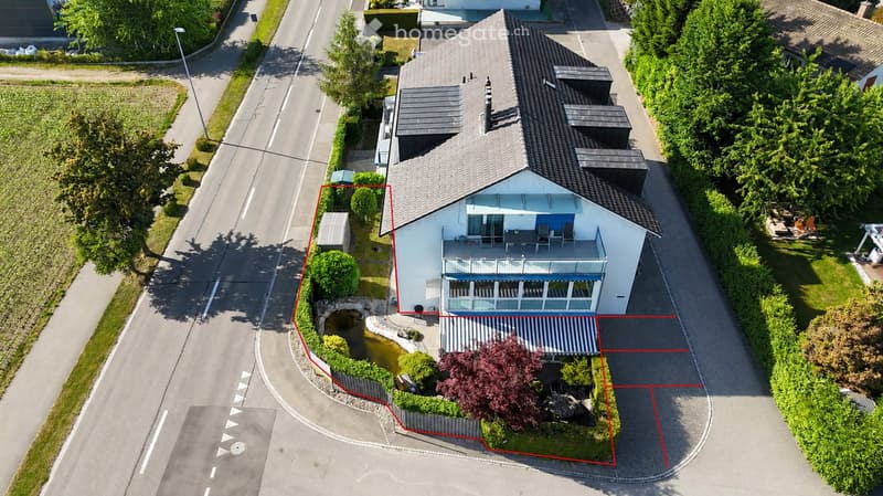 A two-story house with a modern design, featuring a balcony, a small pond in the front yard, and surrounding greenery.