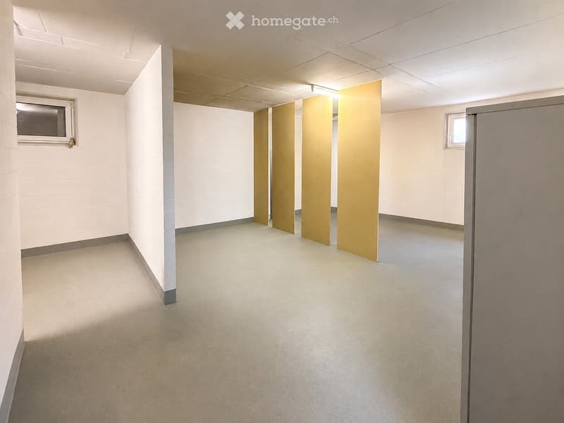 Empty restroom area with beige carpeting, white tiled walls, and multiple stall doors. Windows are present on both sides.
