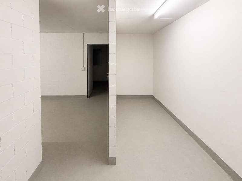 Empty hallway with white brick walls, concrete floor, and a single doorway leading to another room.