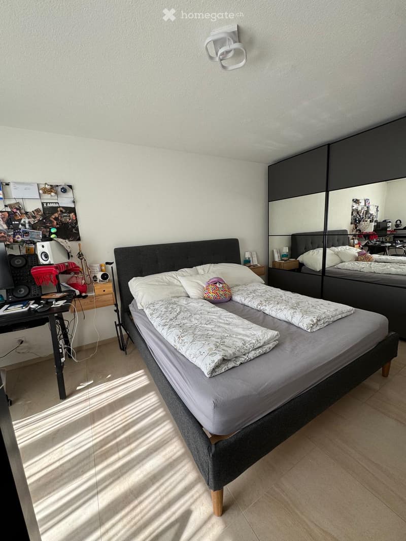 Modern bedroom with a double bed, mirrored wardrobe, desk with chair, and wall-mounted lamp.