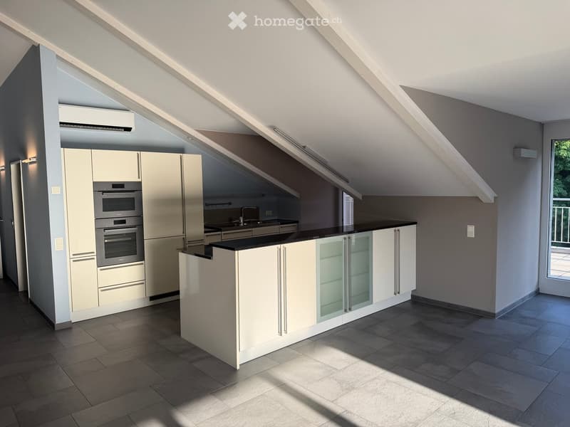 Modern kitchen with white cabinets, stainless steel oven, and a black countertop, featuring a slanted ceiling and large windows.