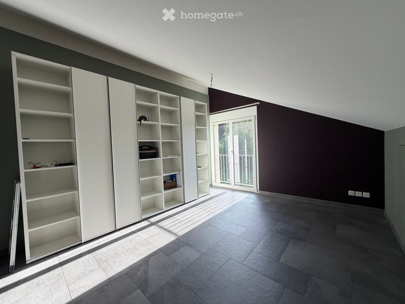 Empty room with white built-in shelving units, dark walls, and a large sliding glass door leading to a balcony.