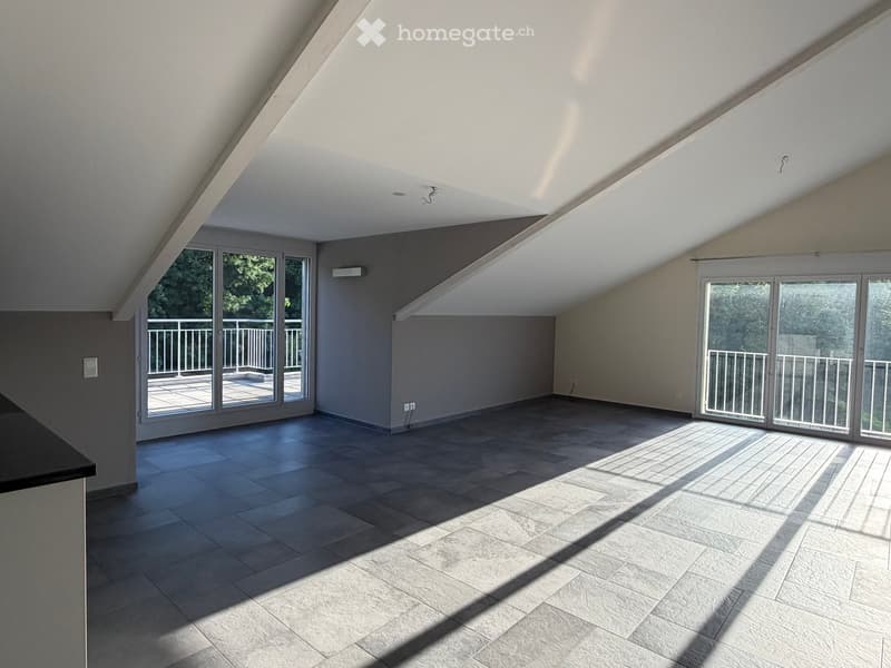 Bright, empty attic room with wooden flooring, large windows, and sliding glass doors leading to a balcony.