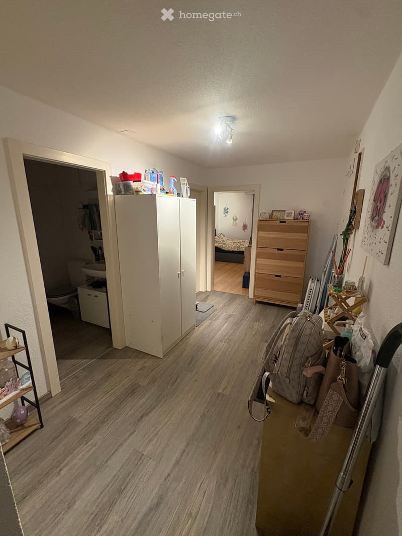 Hallway with wooden flooring, white walls, and several doors leading to other rooms. Visible items include a large wooden dresser, a small shelf with decorative items, and a backpack on the floor.
