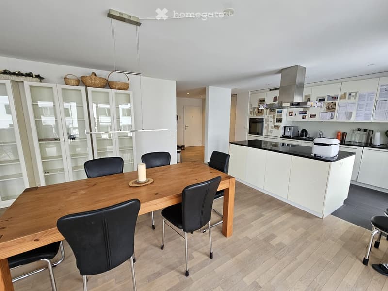 Open-plan kitchen and dining area with white cabinets, black countertops, a wooden dining table with black chairs, and a modern kitchen island.
