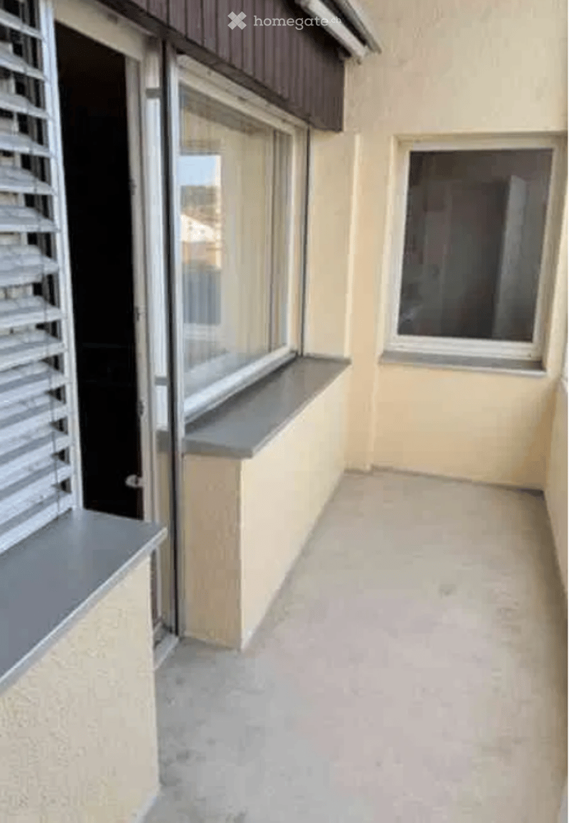 Balcony with beige walls, grey window sills, and a view of the street through the windows.