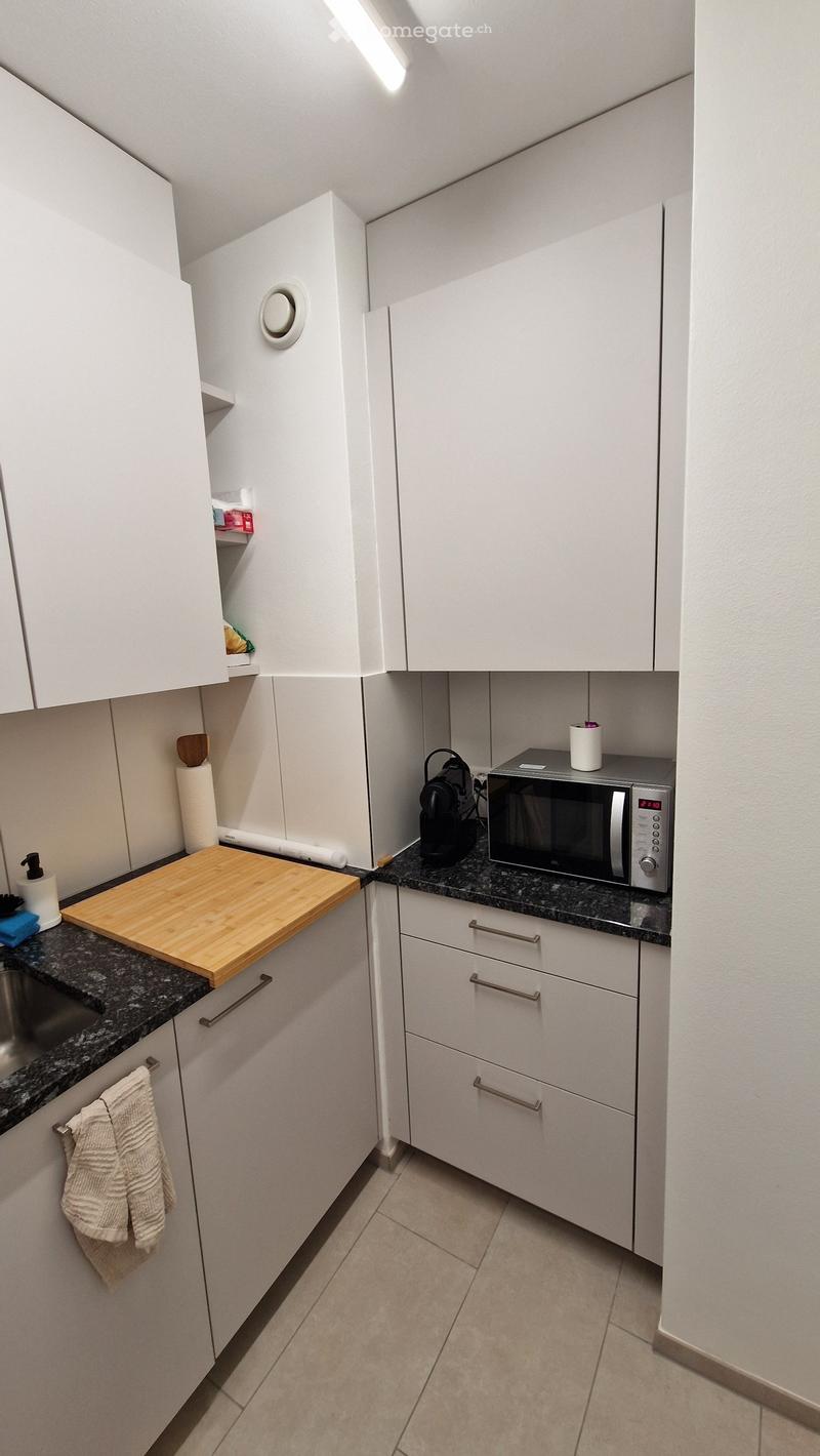 Modern kitchen with white cabinets, granite countertops, microwave, coffee maker, and a wooden cutting board.