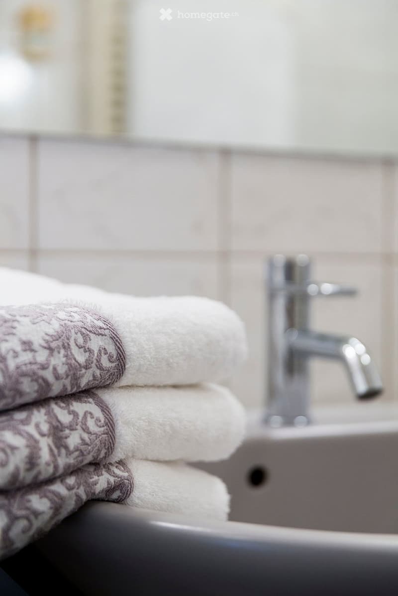 Close-up of a bathroom sink with a modern chrome faucet and neatly stacked towels on the edge of the sink.