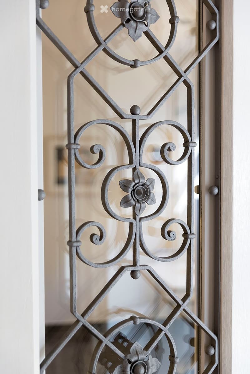 Close-up of an ornate metal door with floral and scrollwork design, featuring glass panels.