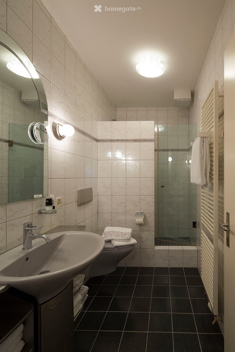 Modern bathroom with marble tiles, a sink with a modern faucet, a toilet, a shower with a glass enclosure, and a radiator with towels.
