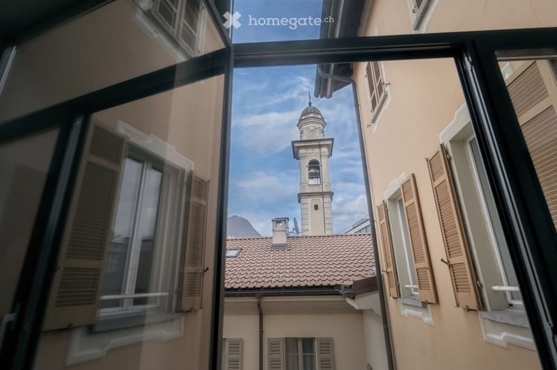 View from a balcony overlooking a narrow street with a church tower and tiled roofs.