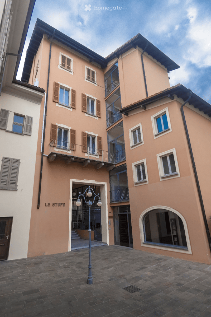 A three-story building with beige walls, multiple windows with shutters, and balconies. The ground floor features an arched entrance and a sign reading "LE STUFE".