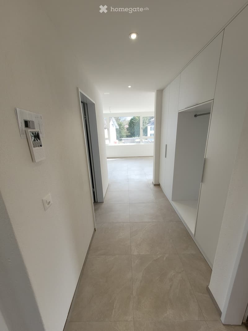 Clean, modern hallway with tiled floor, white walls, built-in closet, and a door leading to a balcony area.