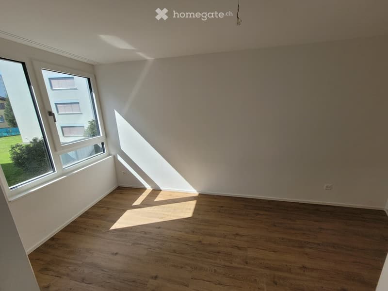 Empty room with wooden flooring and large windows allowing natural light to enter, creating a bright and open space.