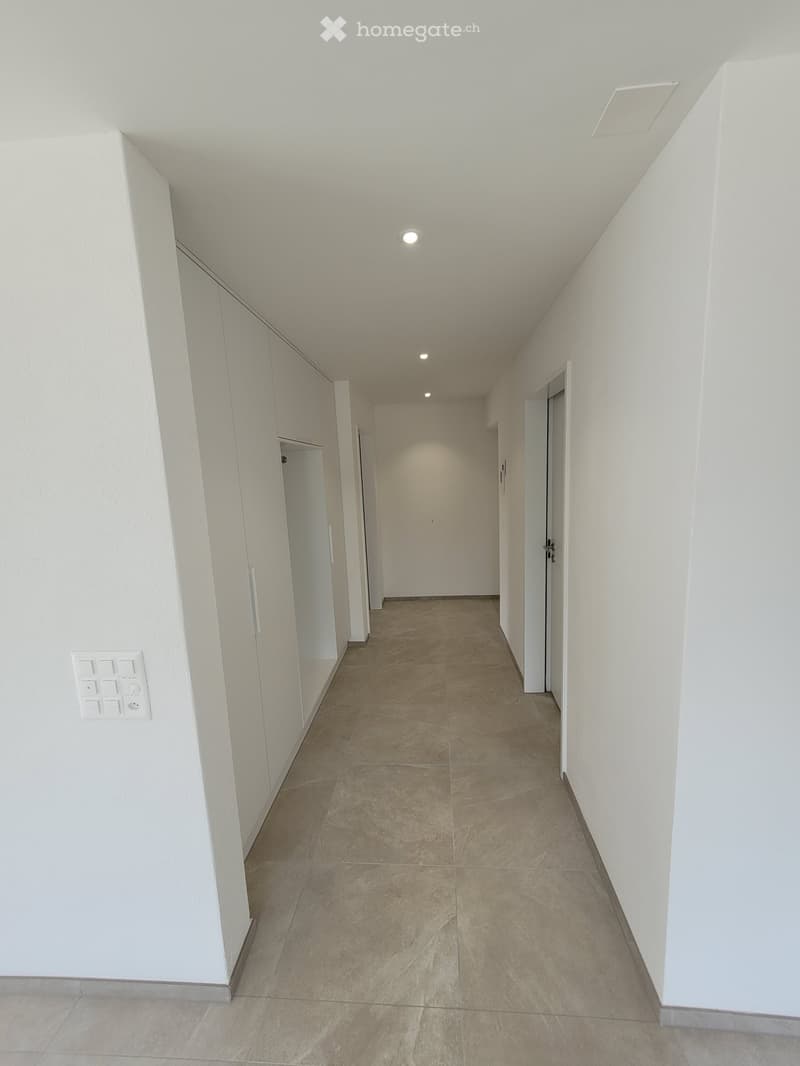 Empty hallway with beige tiled flooring, white walls, and recessed lighting. Doors are visible on both sides.