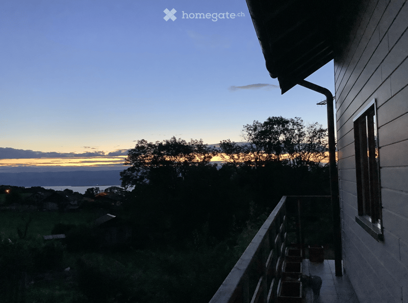 Balcony overlooking a scenic view of a lake and distant hills during sunset, with a few potted plants on the balcony.