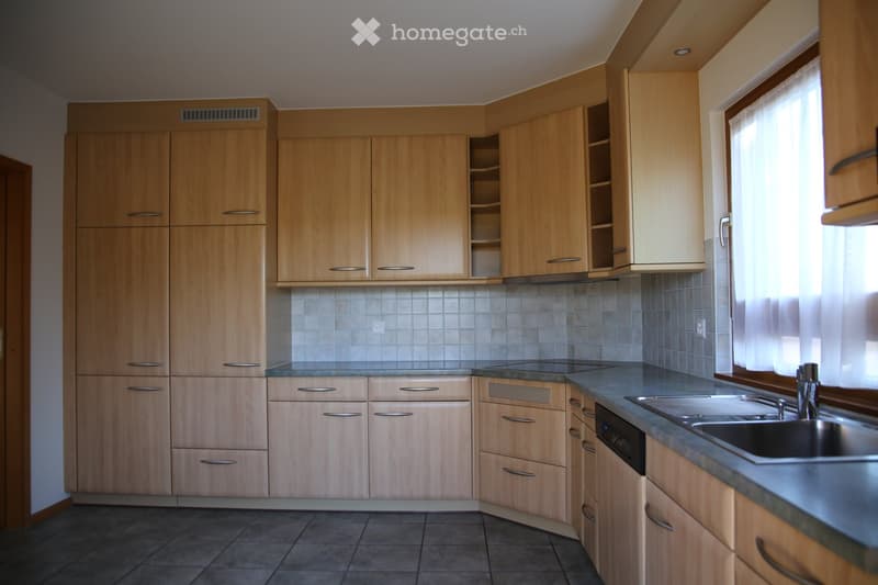 Modern kitchen with light wooden cabinets, stainless steel sink, and dishwasher. The countertops are dark, and the backsplash is tiled.