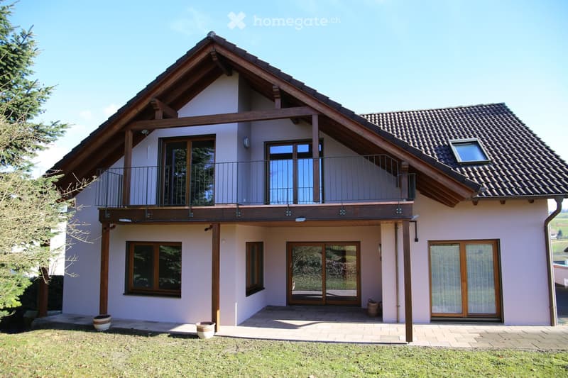 Two-story house with a modern design, featuring a tiled roof, large windows, and a balcony on the upper level.
