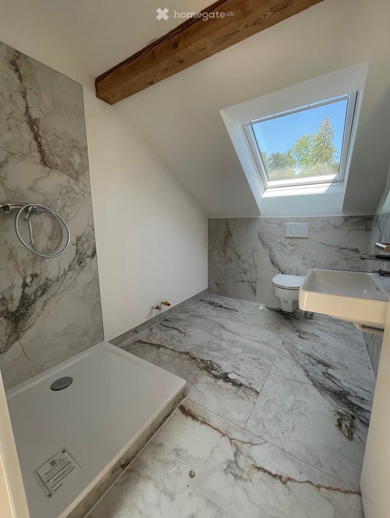 Modern bathroom with marble tiles, a bathtub, toilet, sink, and a skylight window providing natural light.