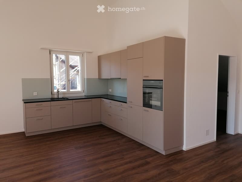 Modern kitchen with light-colored cabinets, a black countertop, and a built-in oven. The space features wooden flooring and large windows.