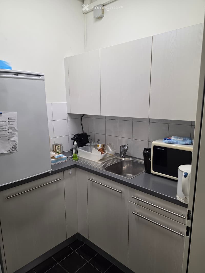 Modern kitchen with white cabinets, stainless steel appliances, and a black countertop. Includes a refrigerator, microwave, sink, and various small appliances.
