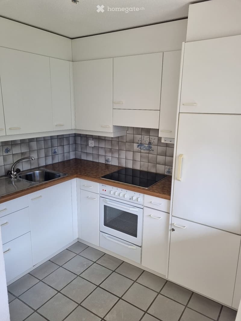 Modern kitchen with white cabinets, wooden countertops, and tiled backsplash. Features a sink, stove, and refrigerator.