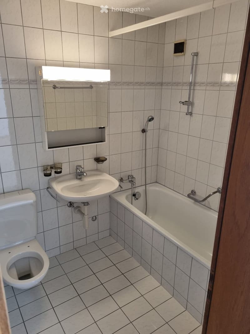 Bathroom with tiled walls and floor, featuring a toilet, sink, bathtub, mirror, and showerhead.