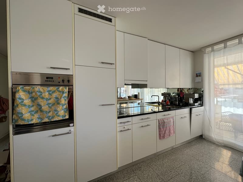 Modern kitchen with white cabinets, stainless steel oven, sink, coffee maker, and a towel hanging on the cabinet.