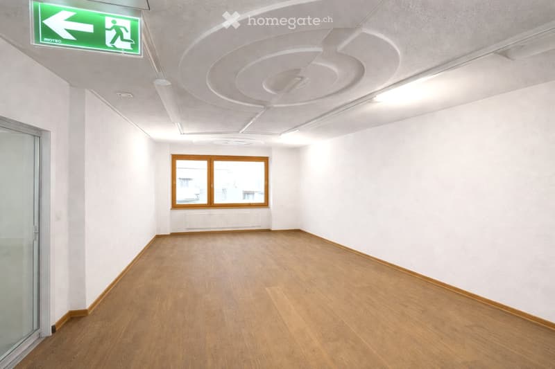 Empty room with white walls, wooden flooring, large windows, and a glass door. No furniture or equipment present.