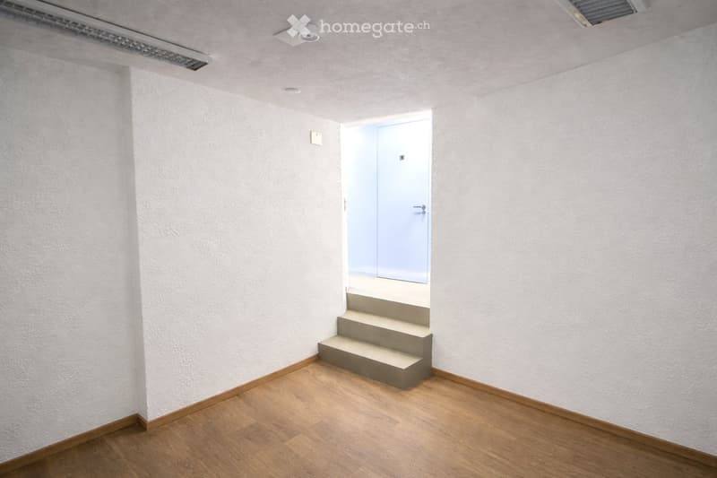 Empty room with light-colored walls, wooden flooring, and a small staircase leading to another area.