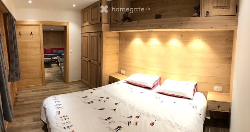 Cozy wooden bedroom with a double bed, nightstand, and an open loft area with a sofa and chairs.