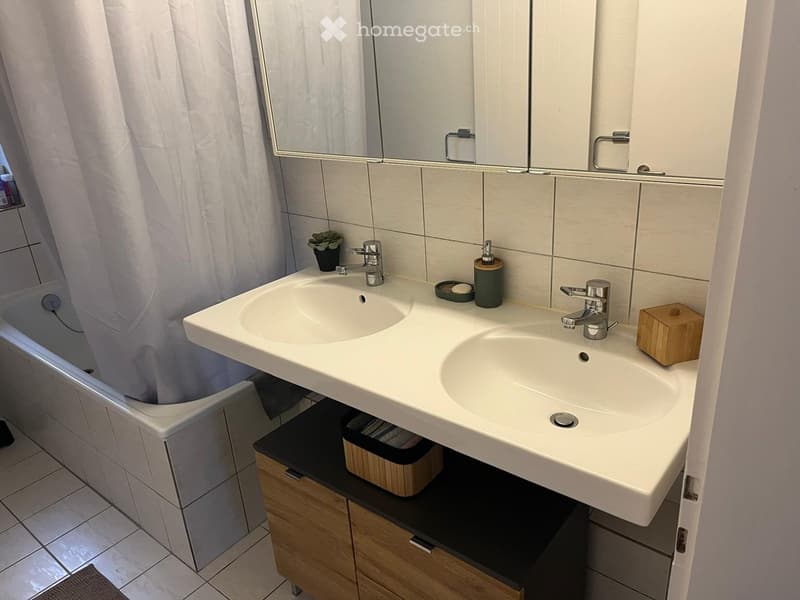 Modern bathroom with double sink, mirrored cabinet, bathtub, and wooden storage cabinet.