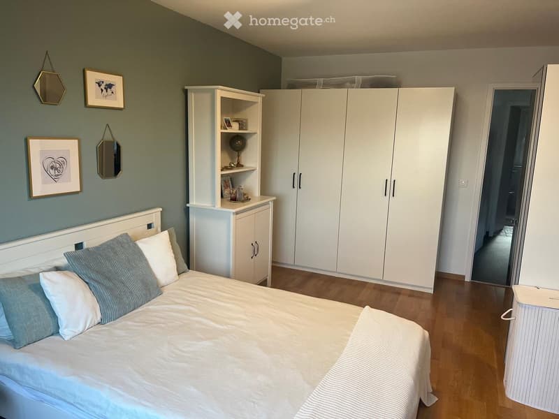 A modern bedroom with a white bed, light blue pillows, a large white wardrobe, and decorative wall mirrors.