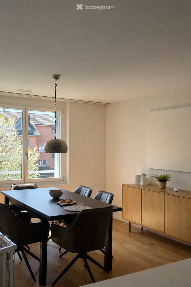 Dining room with a black dining table, four black chairs, a bowl, a plate with fruit, a wooden cabinet, a vase, and a small potted plant on the cabinet.