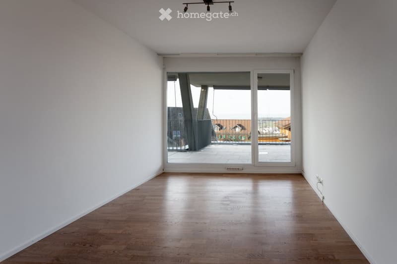 Empty room with wooden flooring, white walls, and a large sliding glass door leading to a balcony.