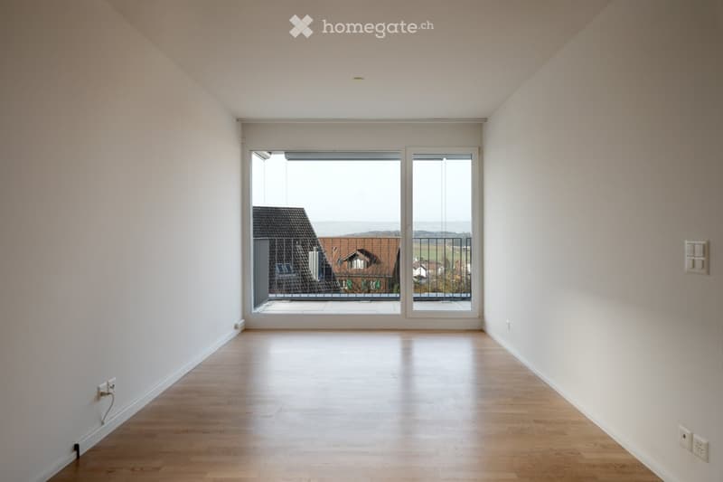 Empty room with wooden flooring, white walls, and large sliding glass doors leading to a balcony.