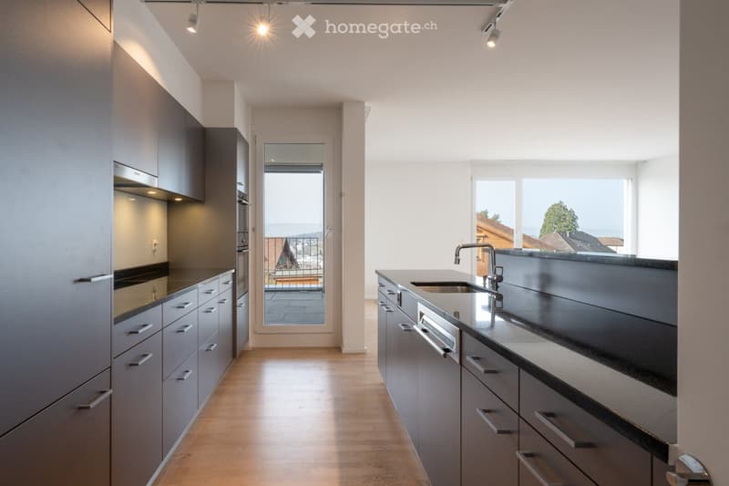 Modern kitchen with grey cabinets, a sink, and an oven, featuring large windows with a scenic view.