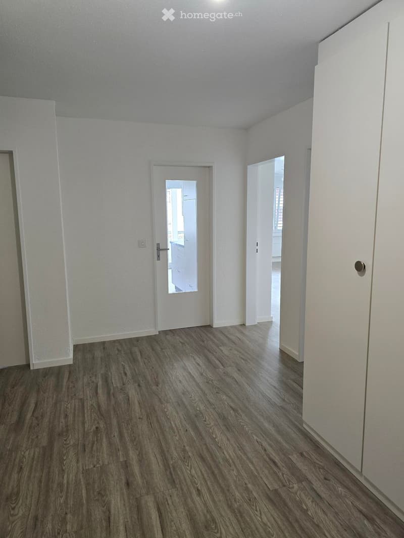 Empty room with wooden flooring, white walls, and two open doors leading to other spaces.