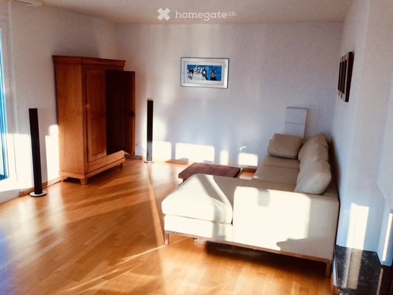 Bright living room with light-colored sofa, coffee table, wooden wardrobe, and floor lamps. Natural light streams in from large windows, creating a warm and inviting atmosphere.