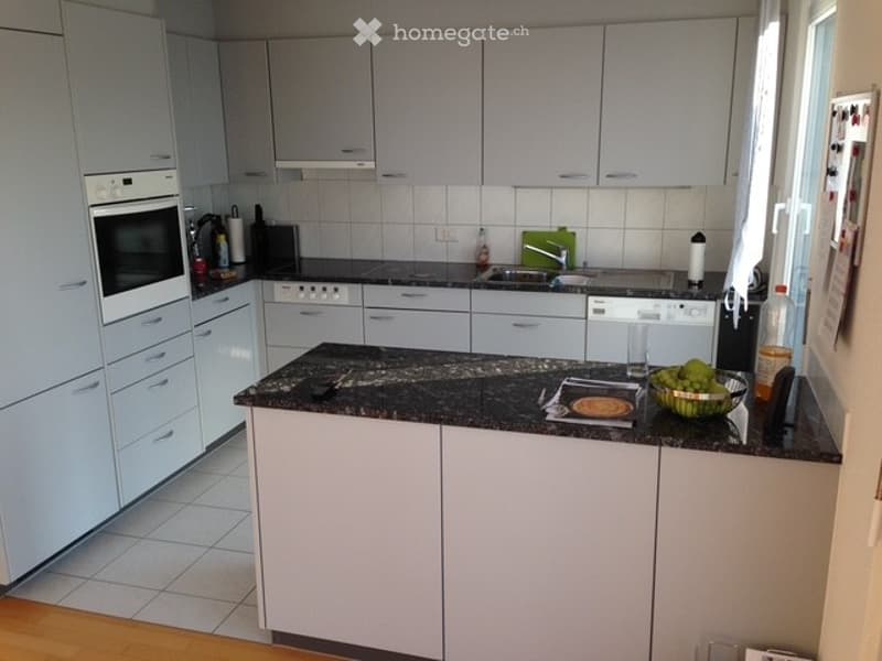 Modern kitchen with white cabinets, granite countertop, built-in oven, dishwasher, and various appliances.