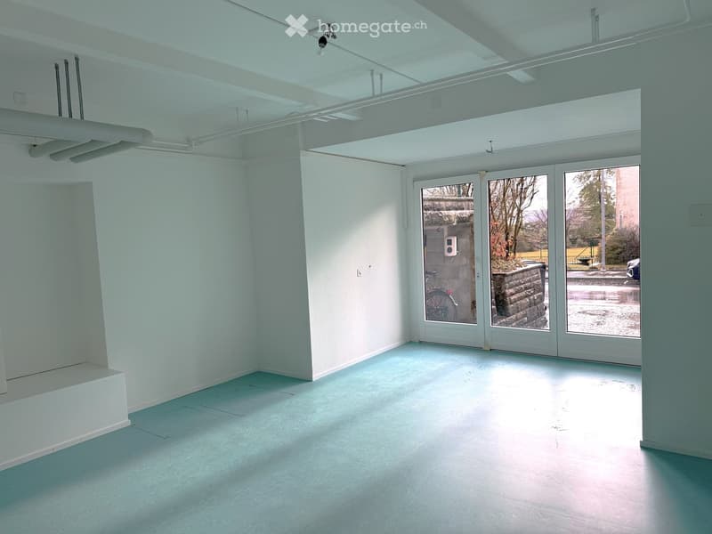 Empty room with light blue walls and floor, large glass sliding doors leading to an outdoor area, visible electrical outlets and exposed ceiling beams.