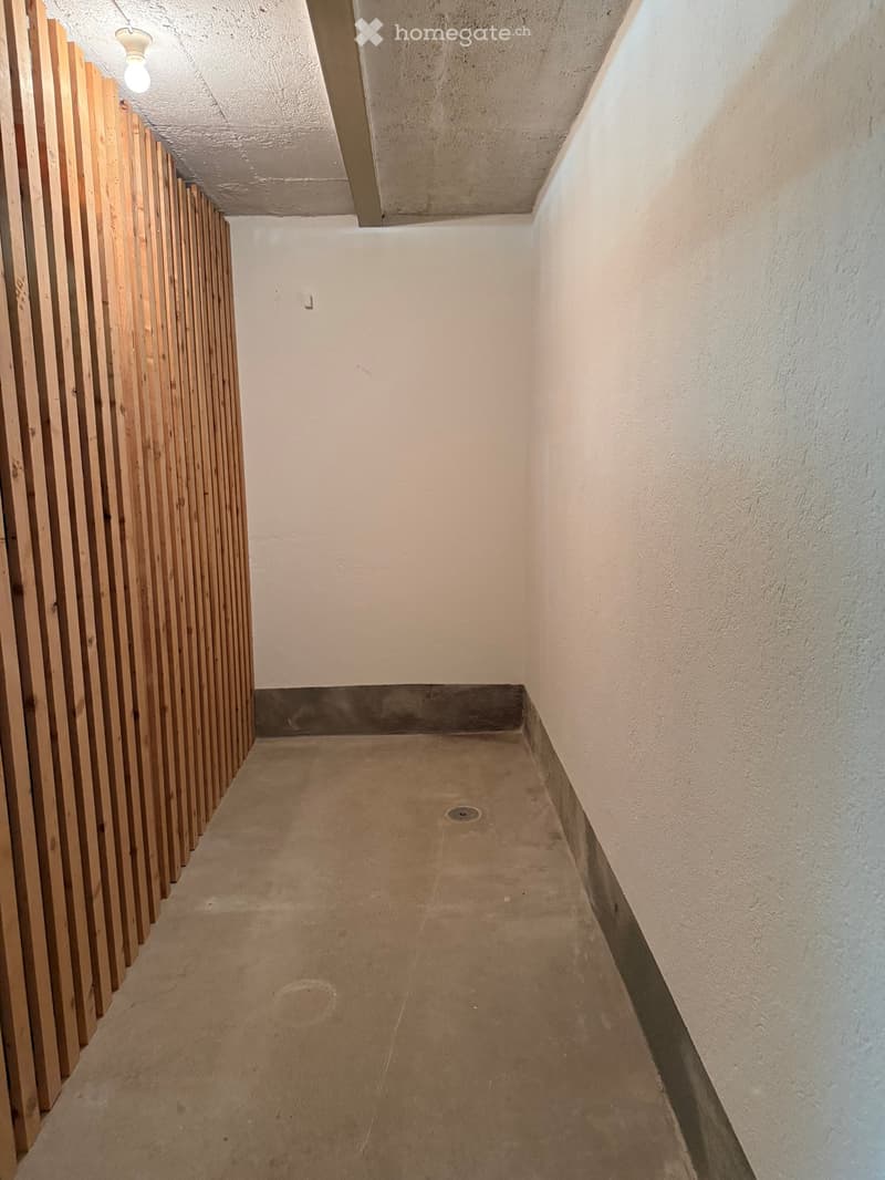 Empty hallway with concrete floor, white walls, and a wooden panel on the left side.