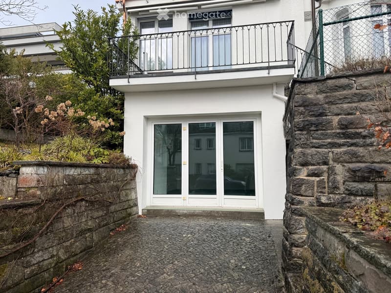 White multi-story building with a balcony, stone steps, and a paved pathway leading to the entrance.