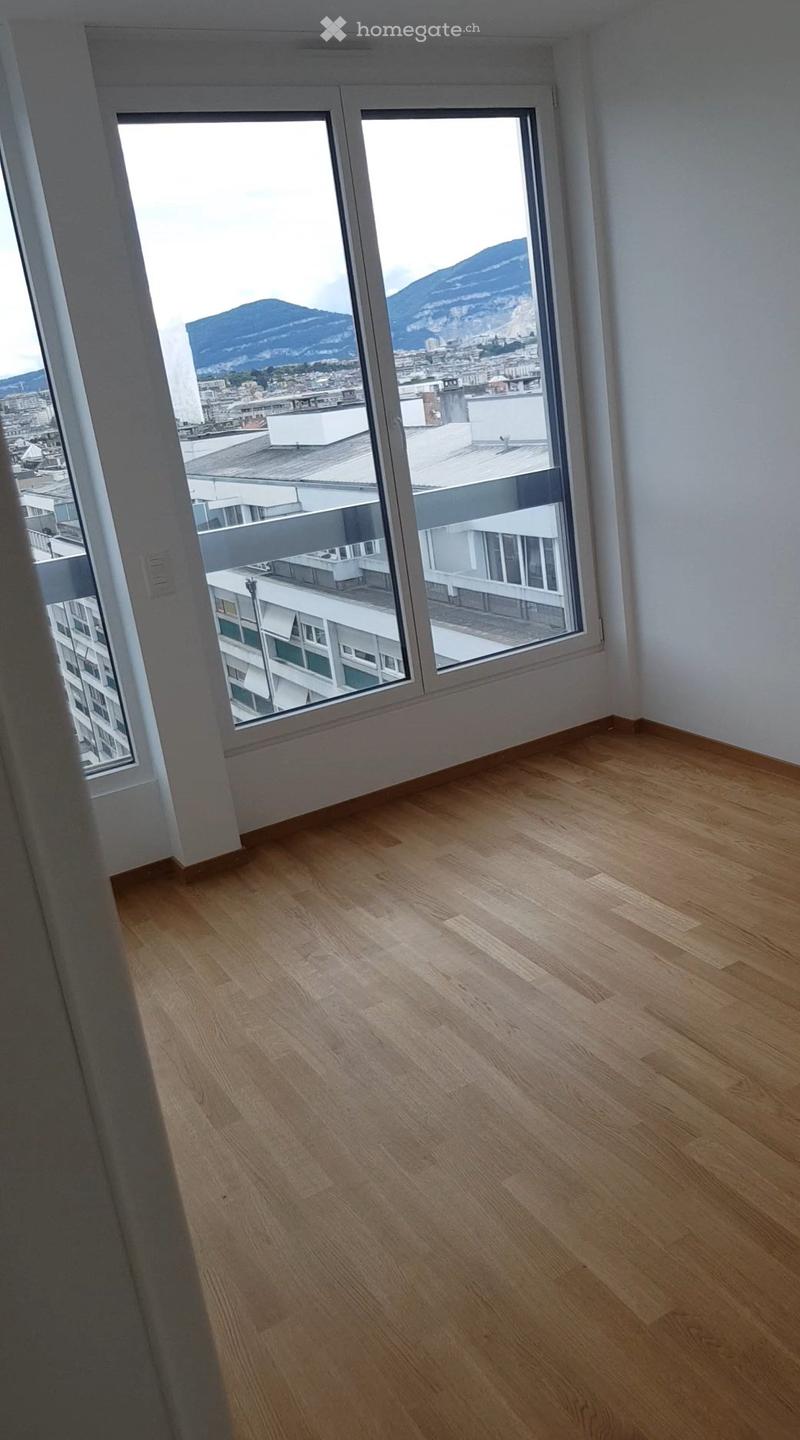 Empty room with light wooden flooring and large windows offering a view of a cityscape and mountains.