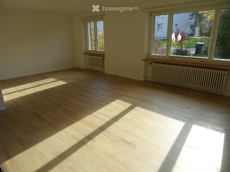 Empty room with light wooden flooring, large windows, radiators, and wooden window sills.