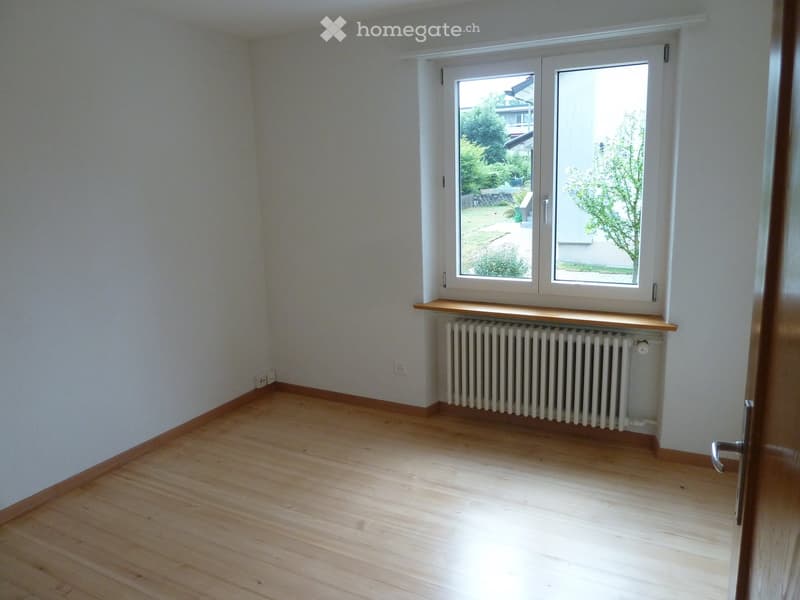 Empty room with wooden flooring, white walls, a radiator, and a window with a wooden sill.